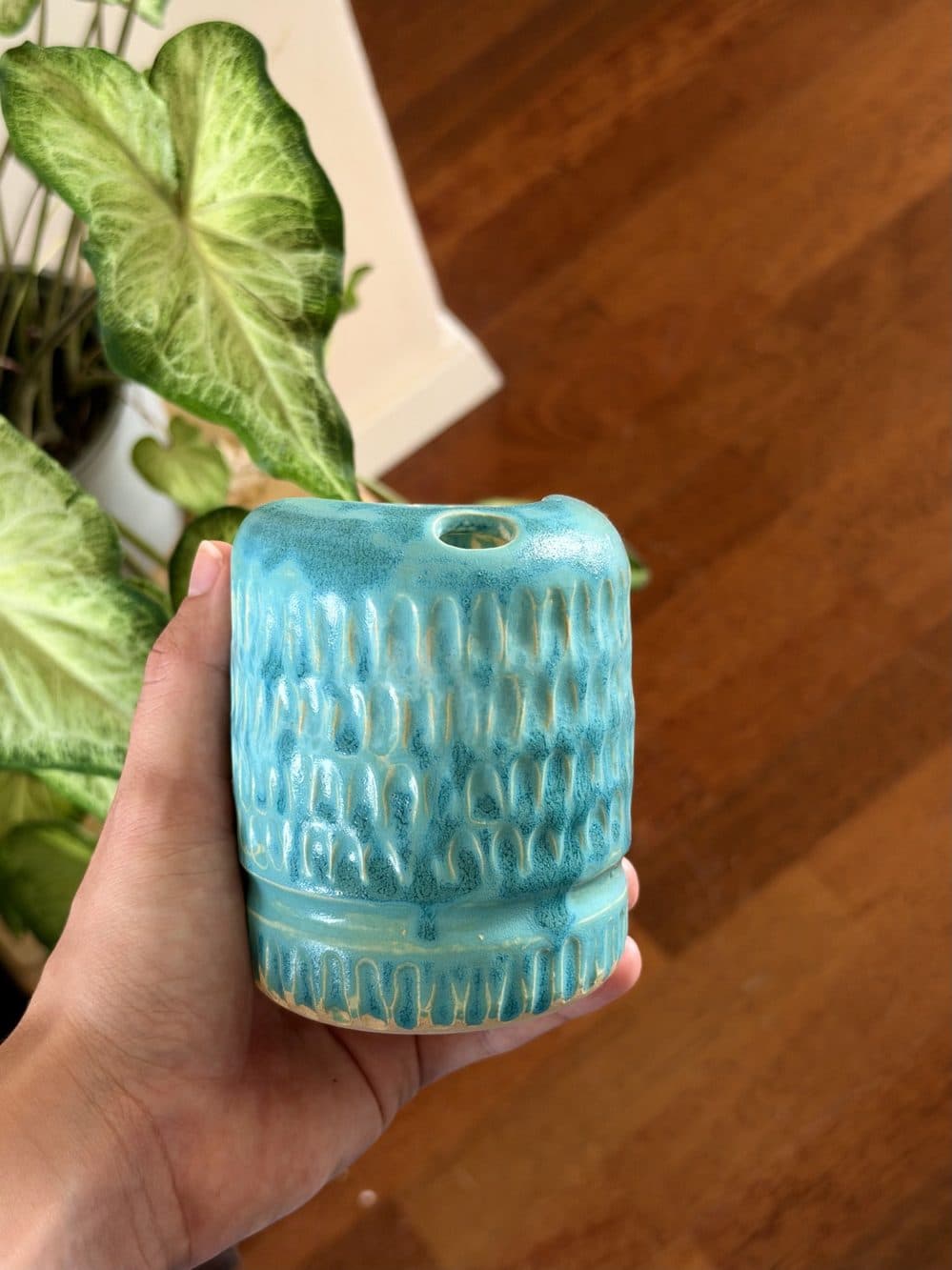 Kleine Vase mit türkiser Glasur und eingeritztem Muster in einer Hand